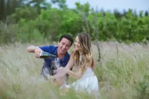 Couple pouring Lokelani sparkling rosé in a grassy field