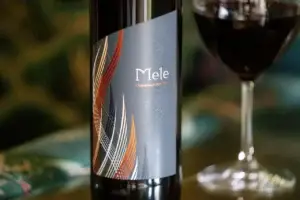 Bottle of Mele red blend beside a glass of red wine