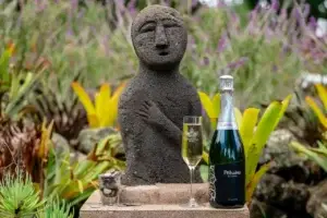 Bottle of Pōhaku sparkling wine beside a stone statue in the garden