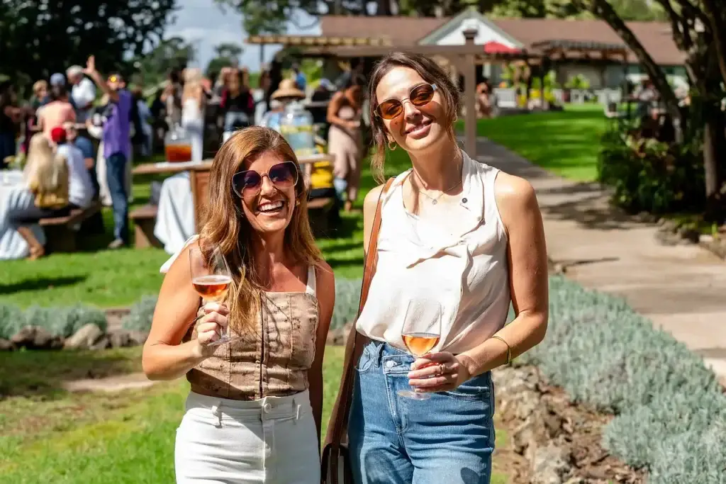 Two friends smiling with wine glasses at a MauiWine event