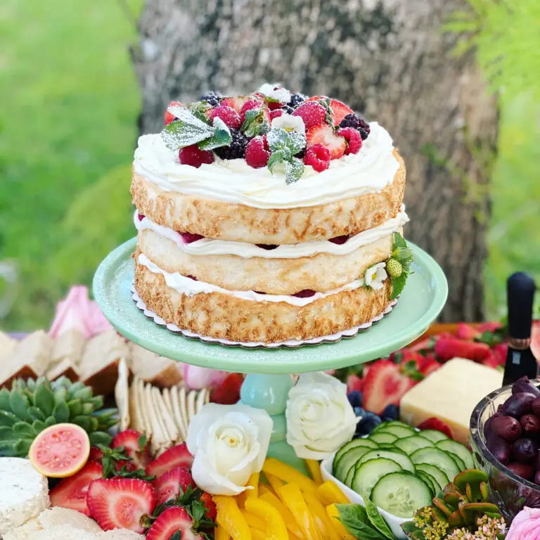 Layered angel food cake topped with fresh berries, flowers and berry sauce on a garden party table