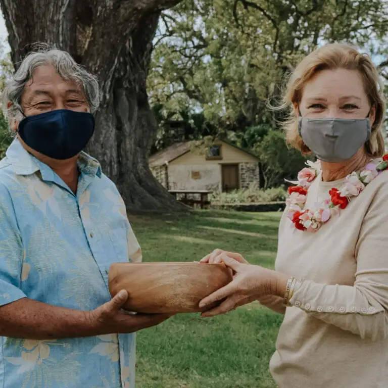 Two MauiWine owners in masks holding the Farm Family of the Year recognition on the winery lawn