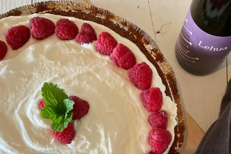 Raspberry cream pie topped with whipped cream, fresh raspberries and mint, with a bottle of Lehua