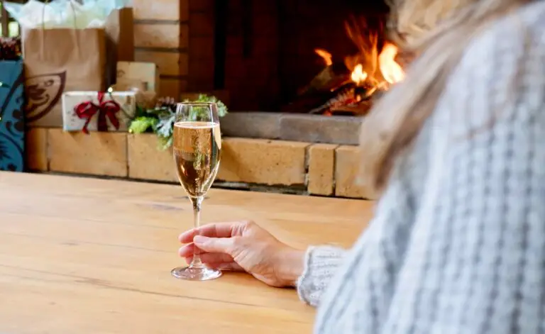 Glass of sparkling wine on a wooden table beside a fireplace and wrapped holiday gifts
